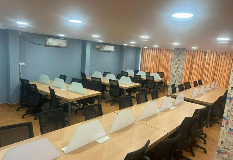 Open-plan office space at Mahatma Gandhi Road featuring multiple wooden desk rows and grey walls.