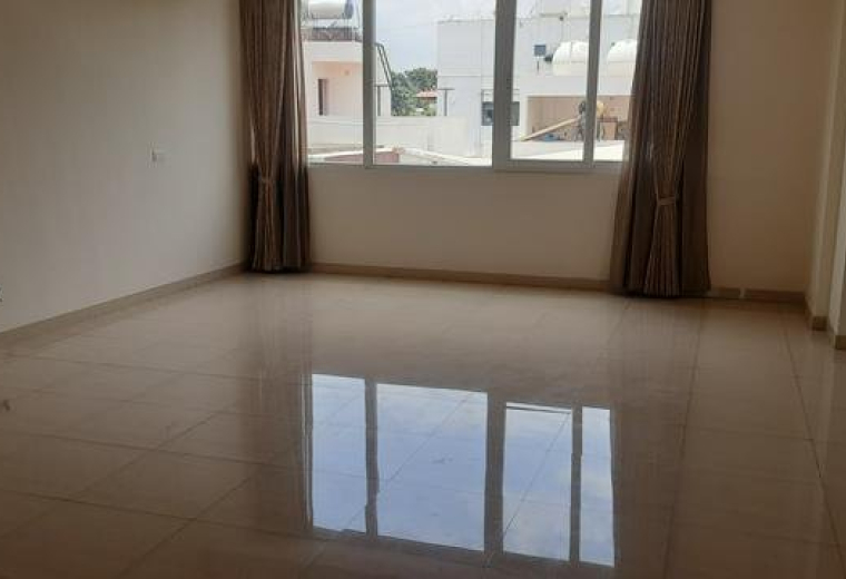 Spacious main hall at Nanda Gokulam with polished tile flooring and natural light from a window.