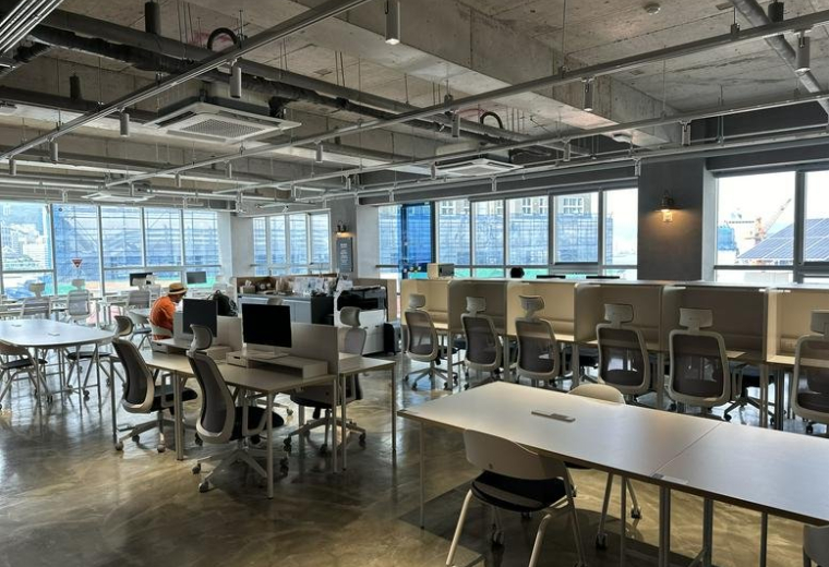 Bright open-plan coworking space with large windows and various seating options.