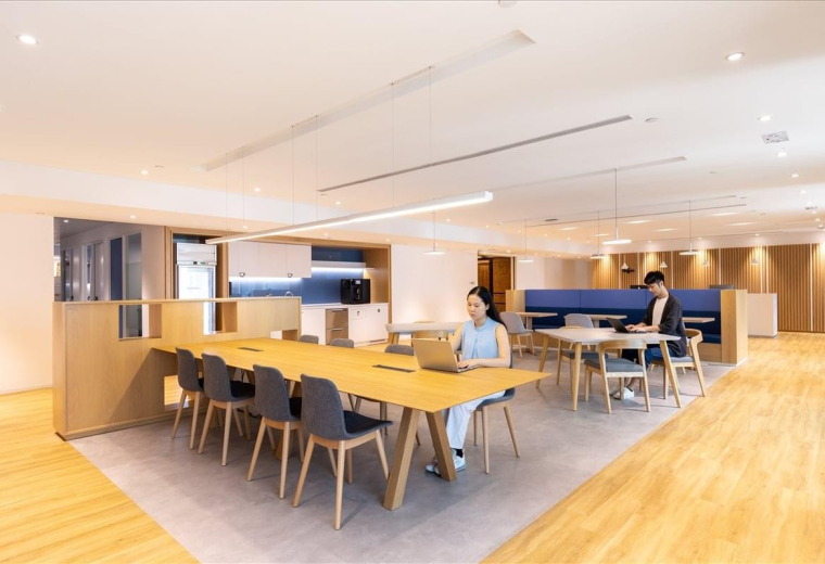 Contemporary coworking space with a long wooden communal table and lounge seating.
