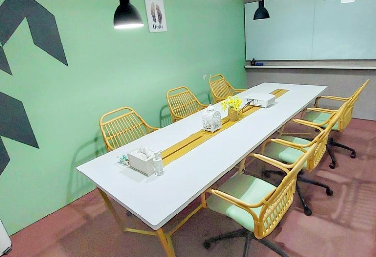 Breakout area with a long white table, woven chairs, and a green wall with geometric patterns.