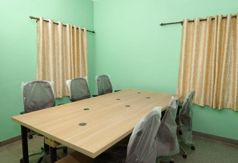Meeting room at 102, Sathy Road, featuring a large wooden table and grey ergonomic chairs against green walls.