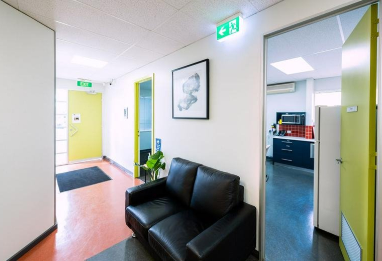 Reception area with a black leather sofa and view into a modern kitchen breakout space.