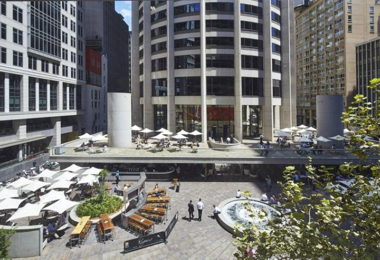 Sun-drenched outdoor plaza with cafe seating and white umbrellas at the base of the tower.