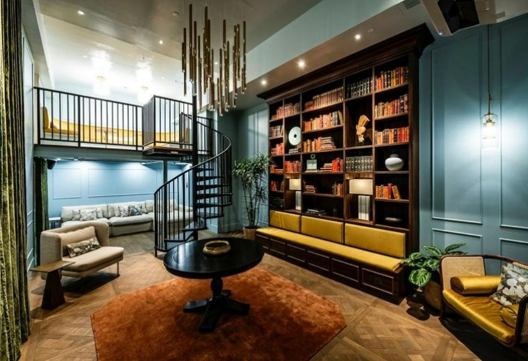 Spacious communal lounge at Eastern Harbour Centre with a spiral staircase, library wall, and warm lighting.