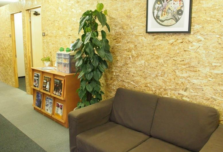 Warm communal lounge area with wood-chip walls, a brown sofa, and a tall green plant.