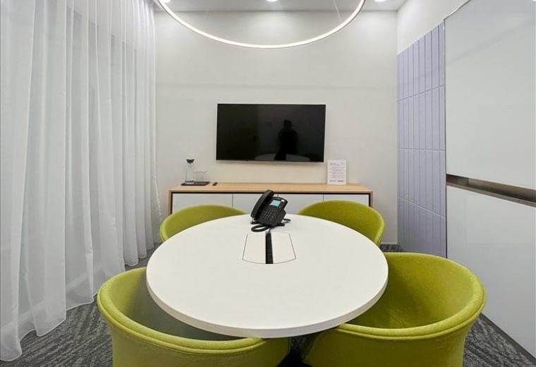 Small private meeting room featuring lime green tub chairs and a circular white pedestal table.
