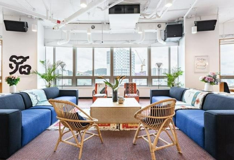 Spacious lounge area with blue sectional sofas, wicker chairs, and large windows overlooking the city.