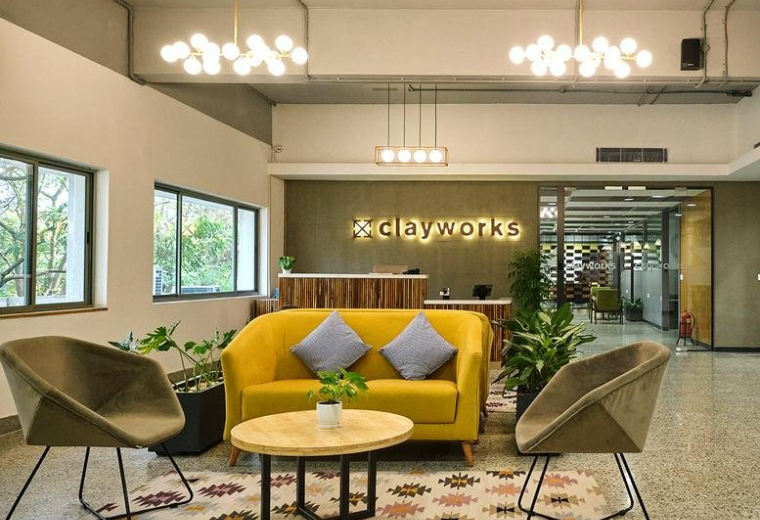 Spacious reception and lounge at Create Campus with a yellow sofa, potted plants, and modern globe chandeliers.