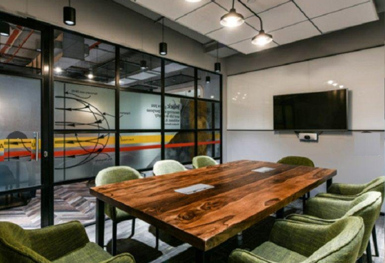 Meeting room at Augusta Point (L2 & L3), Sector 53 Golf Course, Gurugram with a live-edge wood table and green armchairs.