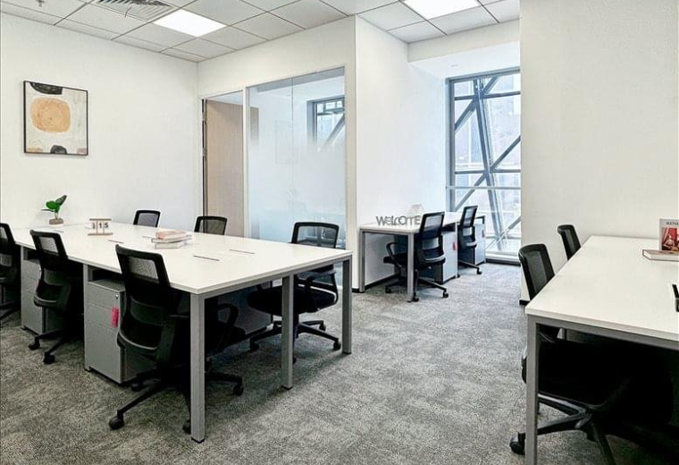 Bright workspace with multiple desks near a large window showing building architecture.