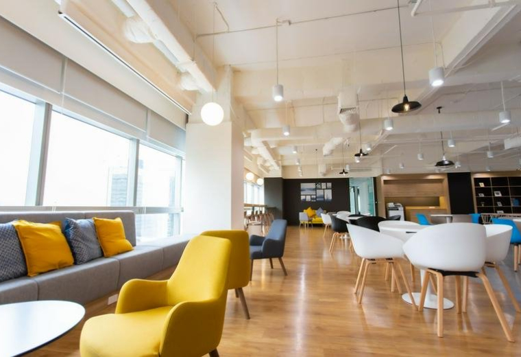 Vibrant office lounge with yellow armchairs, a grey sofa, and city views through large windows.