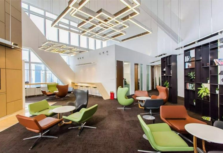 Expansive coworking lounge with mixed colorful seating and geometric overhead lighting.