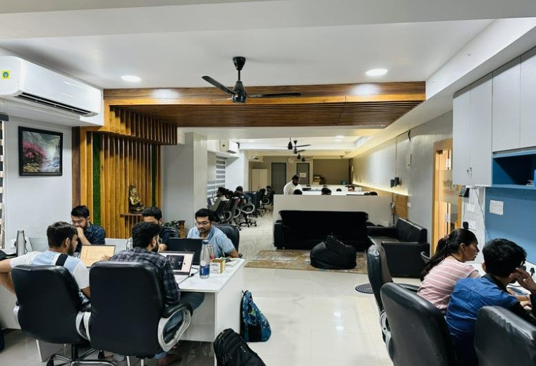 Collaborative office environment featuring wooden ceiling accents and black ergonomic chairs.