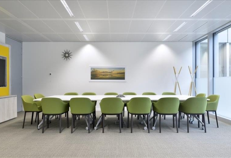 Bright meeting room with a long white table and green chairs.