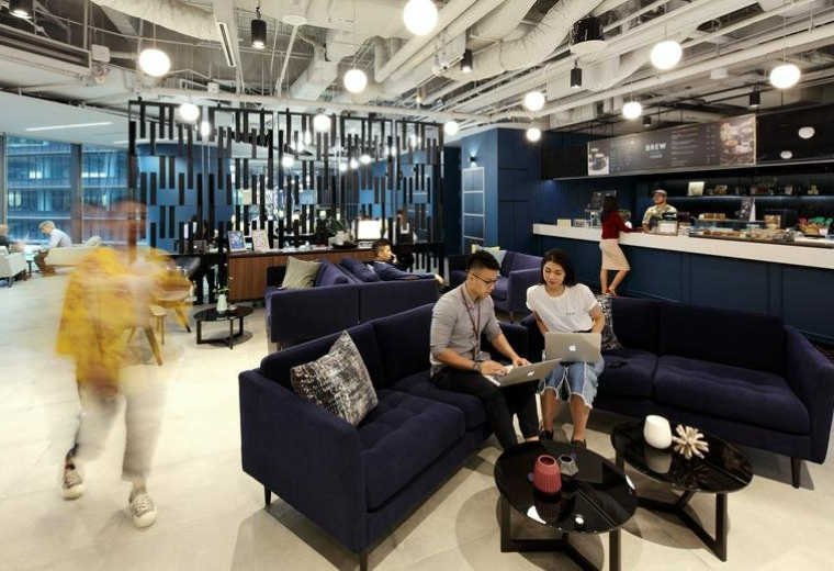 Spacious communal lounge and cafe area at Marina One East Tower with modern blue velvet sofas and industrial ceilings.