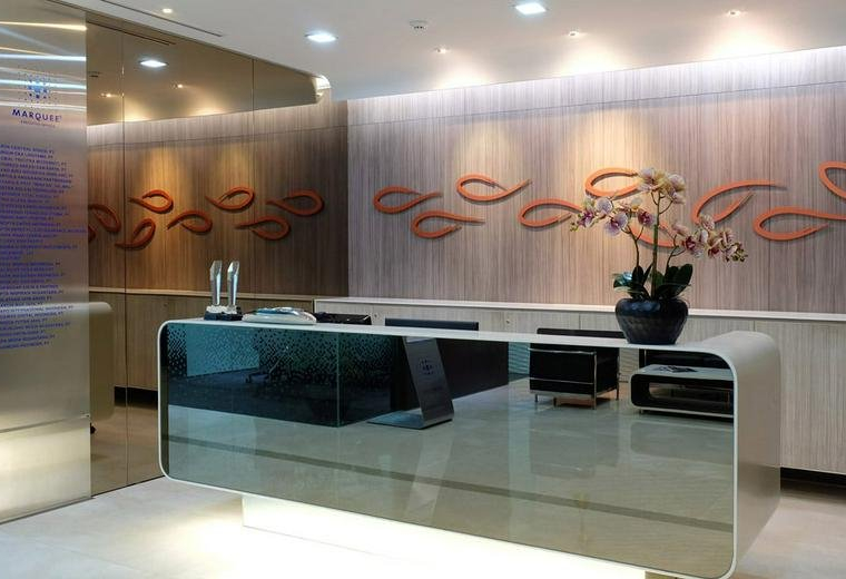 Modern reception desk with a reflective surface and a wooden feature wall with fish motifs.