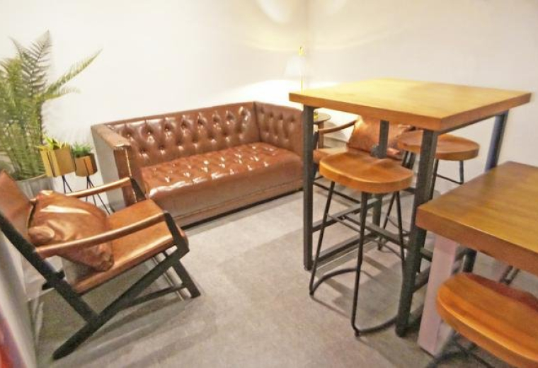 Lounge area at Eton Tower with brown leather sofa, high wooden table, and potted fern.