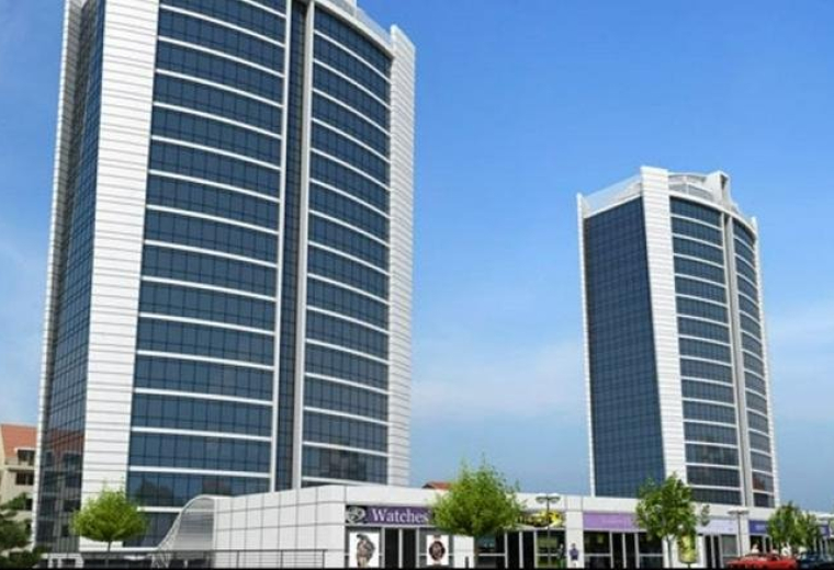 Exterior view of the twin glass-facade Hukukçular Towers under a clear blue sky.