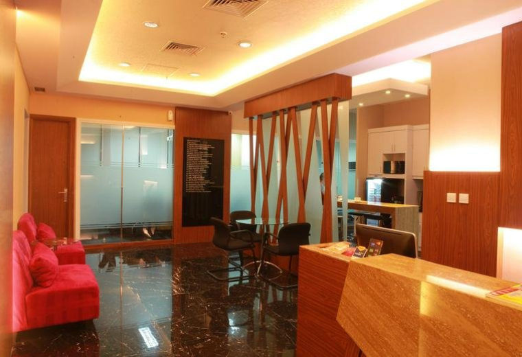 Warm, modern reception area at Kirana 2 Tower with a wooden front desk and plush red sofa.