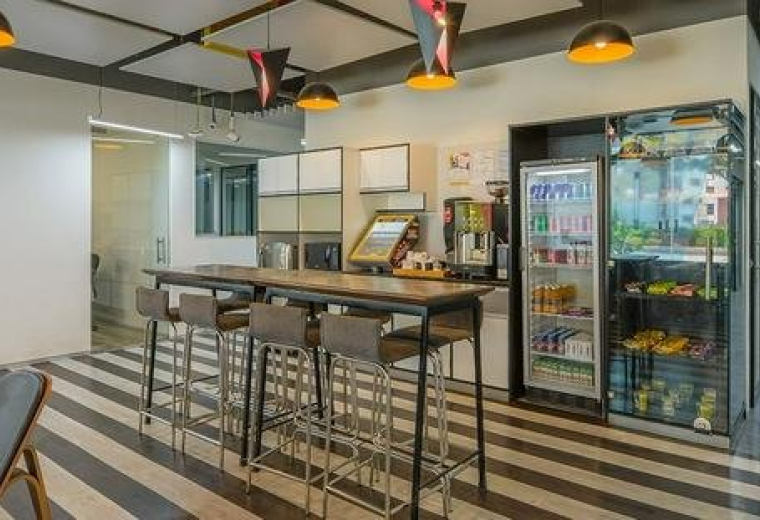 Spacious communal lounge and kitchen area at Modi House Dalia Industrial Estate with high tables and striped flooring.