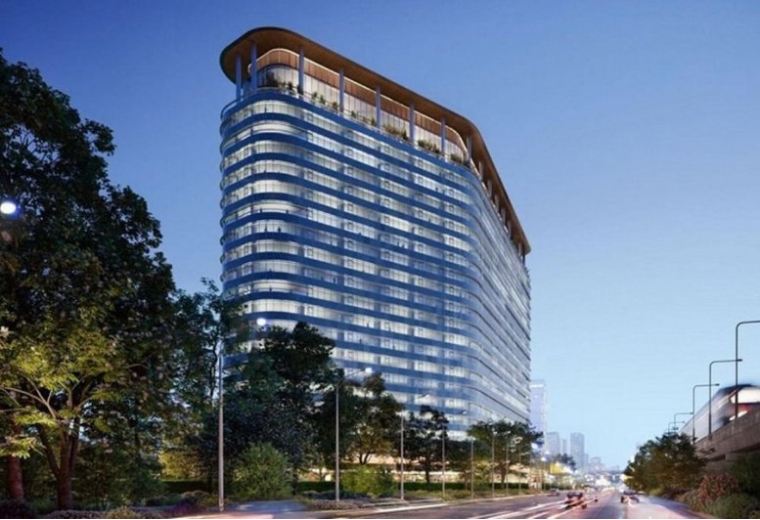 Curved glass office tower illuminated at dusk, with trees and a busy road in the foreground.