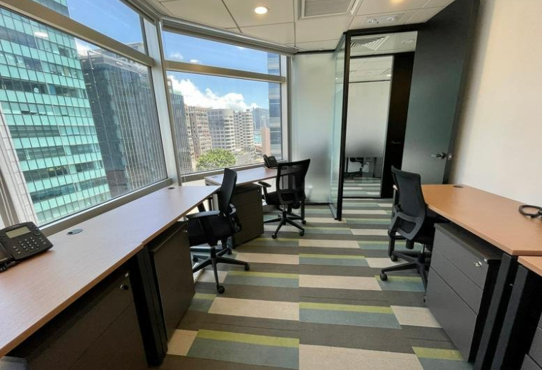 Bright office space with corner windows offering city views and a patterned carpet.