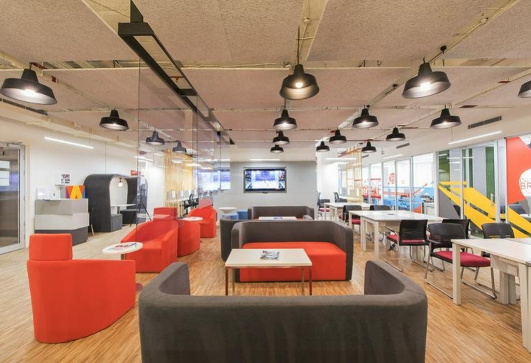Spacious communal lounge featuring vibrant red chairs and warm overhead lighting.