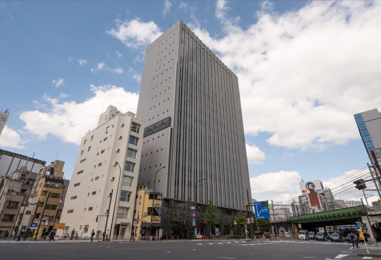 Exterior view of the tall, grey facade of Shinbashi Tokyu Bldg under a blue sky.