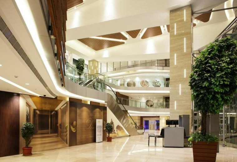 Grand multi-level lobby of The Capital building with warm lighting, indoor trees, and modern architectural details.