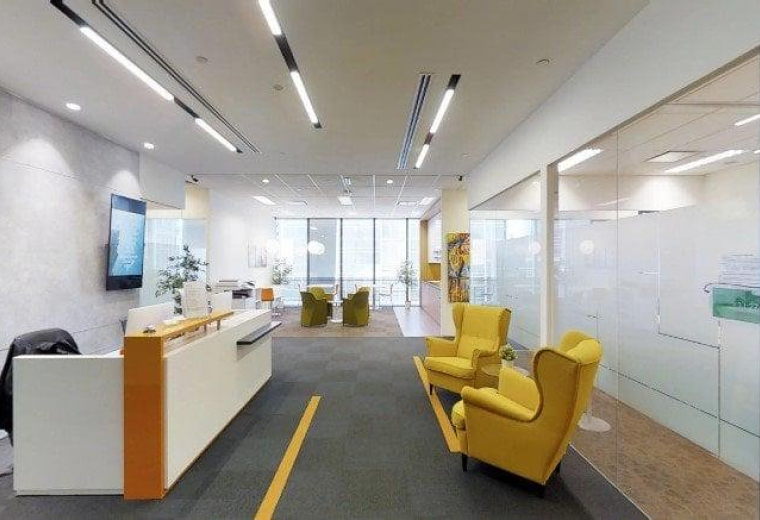 Modern reception desk at Tokio Marine Centre with bright linear lighting and yellow armchairs.