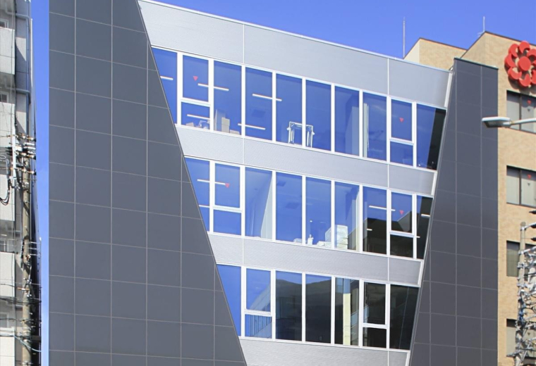 Exterior view of the contemporary Yamato Bldg featuring grey cladding and large glass windows.