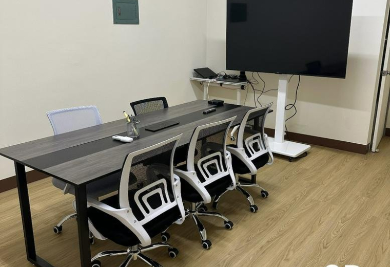 Modern conference room with a dark wood table, several white mesh chairs, and a large flat-screen TV.
