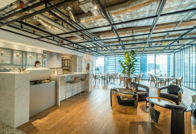 Spacious lounge at One Island East, Level 23 & 60, featuring a modern cafe, wood floors, and floor-to-ceiling windows.