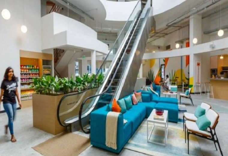 Modern multi-level lobby at Panchshil Futura with an escalator, teal sofas, and indoor plants.
