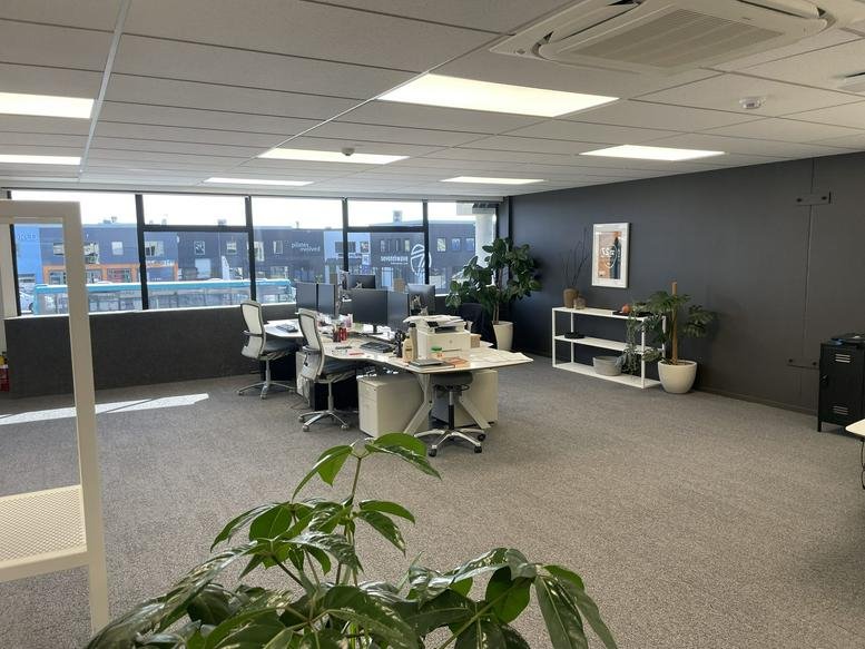 Spacious open-plan workspace at 1020D, Ferry Road, Ferrymead with desks, plants, and large windows.