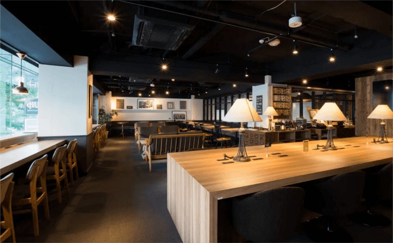 Spacious communal lounge at 2-19-3 Shimbashi, 2F Kashikei Building with warm lighting and wooden tables.