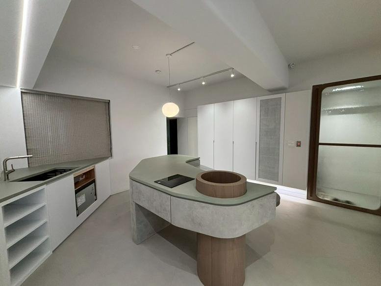 Modern communal kitchen at 2 F. , No. 201-1, Jinhua St. with a unique curved concrete island and minimalist cabinetry.