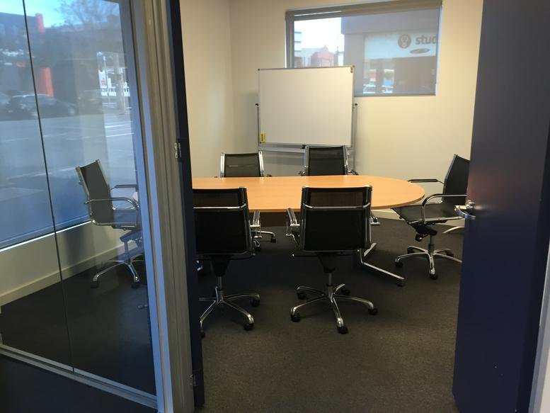A professional boardroom at 460, City Road, featuring a wooden table, black chairs, and a whiteboard.
