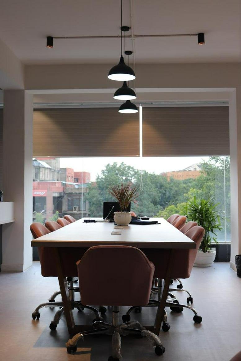 Spacious boardroom with a long white table, pink chairs, and modern pendant lighting.