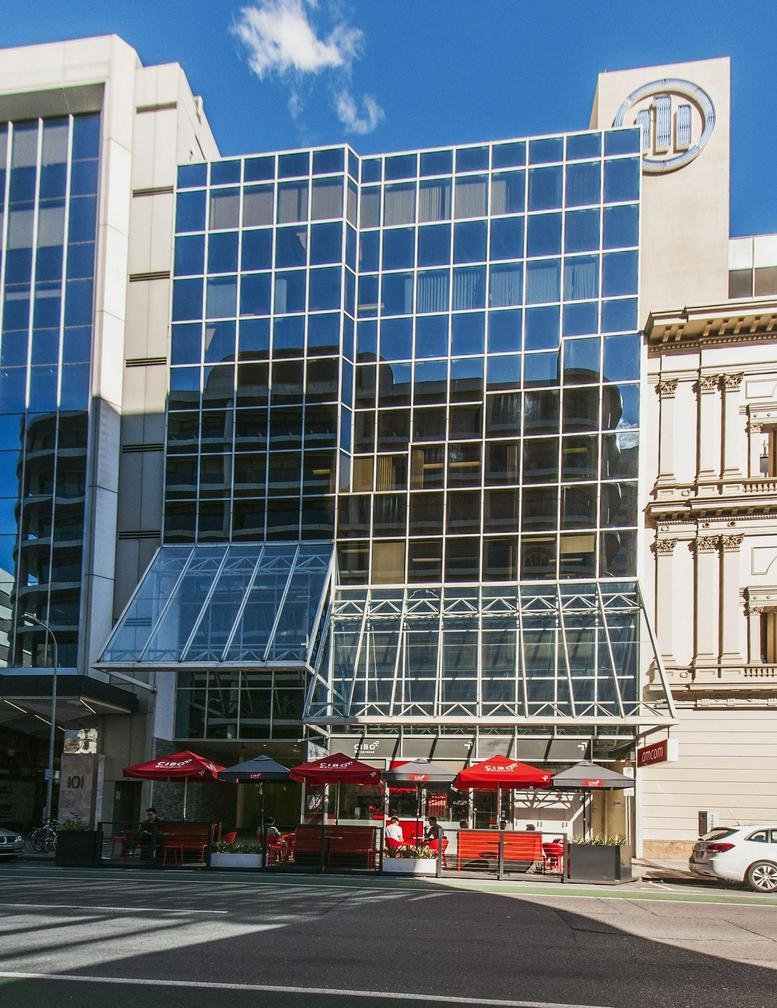 Exterior view of the blue glass-facade building at 97 Pirie Street featuring ground-floor cafe seating.