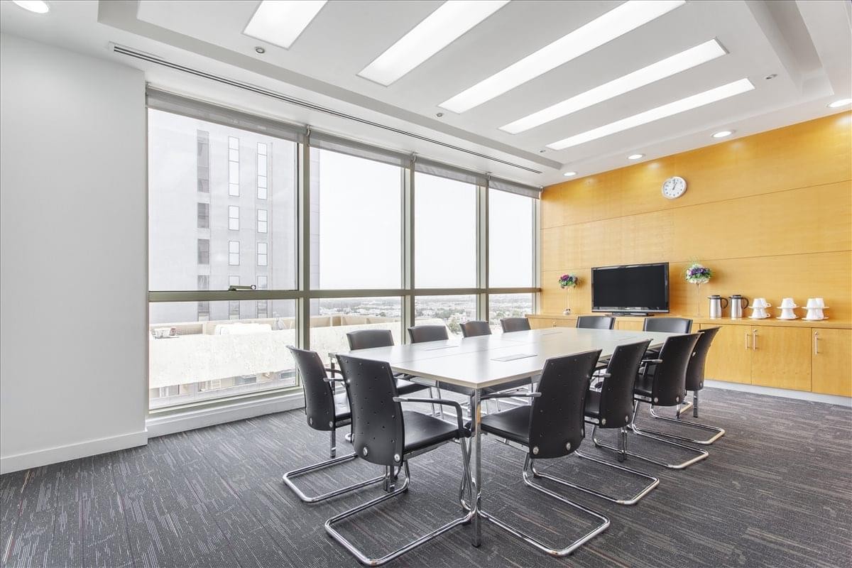 Professional boardroom with a long white table, black ergonomic chairs, and a wood-paneled wall.