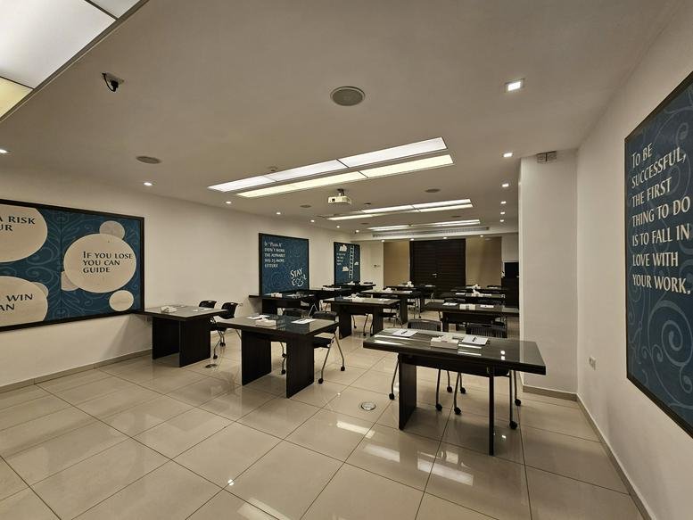 Spacious training room at Al Jama'a Street with several black tables and inspirational wall art.