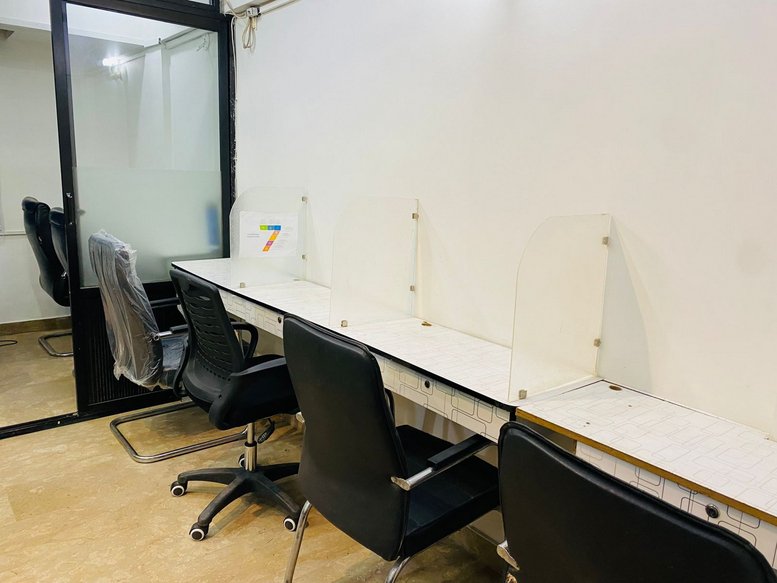 Internal shared workspace at Baradari Apartments, A-20 featuring a row of white desks and black office chairs.