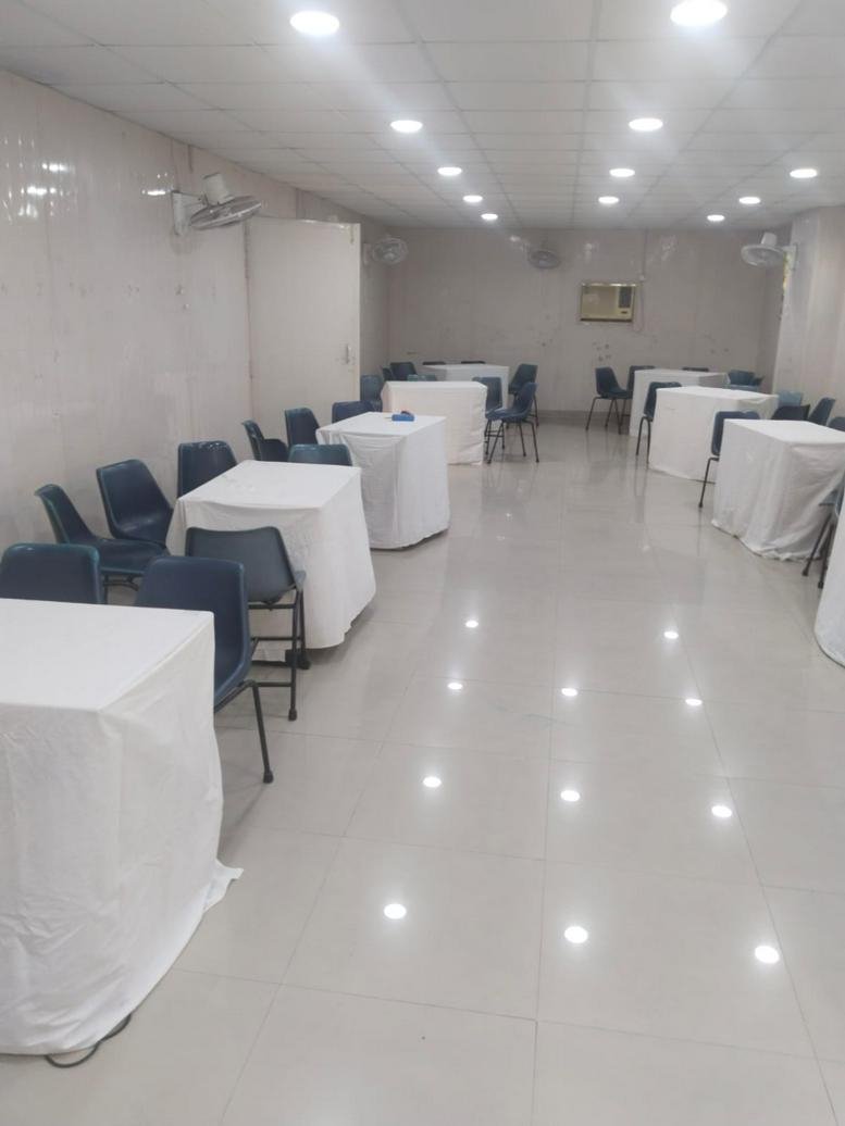 Spacious communal event space at BCS PITAMPURA, Police Lines with white cloth-covered tables and blue chairs.