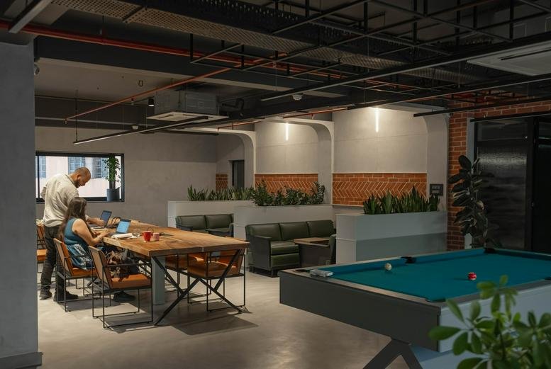 Spacious breakout area with a pool table, wooden communal desk, and green leather sofas.