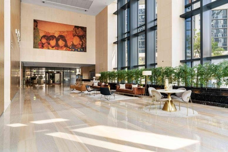 Spacious, sunlit lobby at Boulevard Plaza Tower 1 featuring a large mural, plants, and high ceilings.
