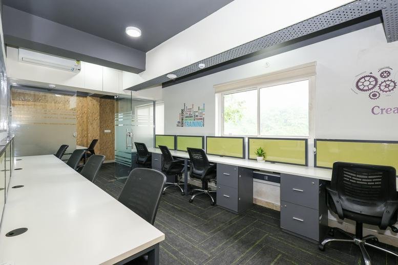 Spacious open-plan workspace at Anand Arcade with white desks, ergonomic chairs, and green partitions.