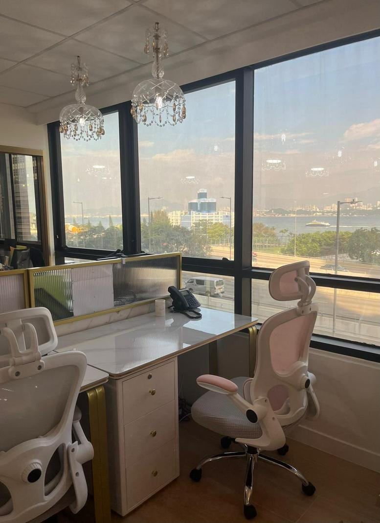 Close-up of a modern workstation with a white desk, pink-accented chair, and a view of the water.