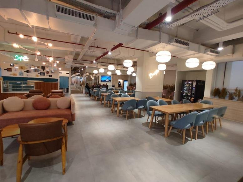 Modern cafeteria at 101, Mathura Road, NH-19, CRRI, Ishwar Nagar, Okhla, Delhi with blue chairs and warm lighting.